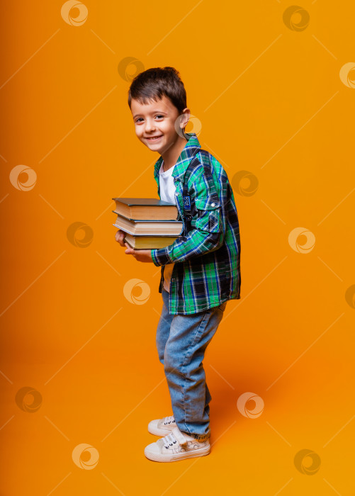 Скачать Счастливый маленький мальчик, держащий в руках Тяжелые книги на изолированном желтом фоне. Концепция образования фотосток Ozero