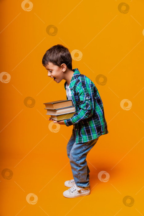 Скачать Счастливый маленький мальчик, держащий в руках Тяжелые книги на изолированном желтом фоне. Концепция образования фотосток Ozero