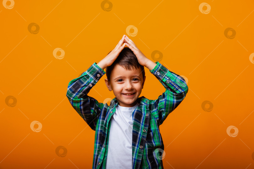 Скачать Изображение мальчика крупным планом, держащего две руки над головой и делающего жест в сторону крыши, на желтом фоне. фотосток Ozero