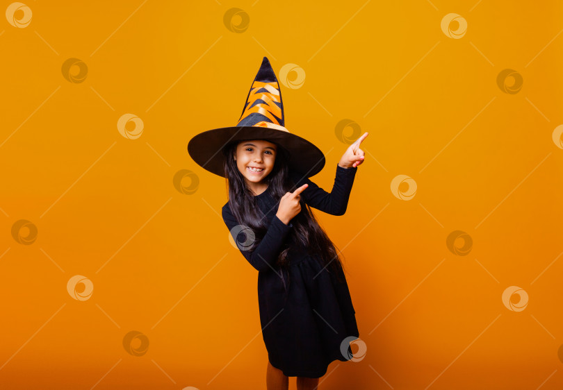 Скачать Маленькая веселая кавказская девочка в костюме ведьмы на Хэллоуин указывает пальцем в сторону. фотосток Ozero