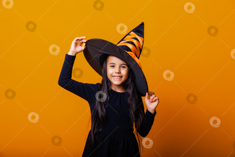 Скачать Маленькая веселая кавказская девочка в костюме ведьмы на Хэллоуин, выделенная на желтом фоне. фотосток Ozero