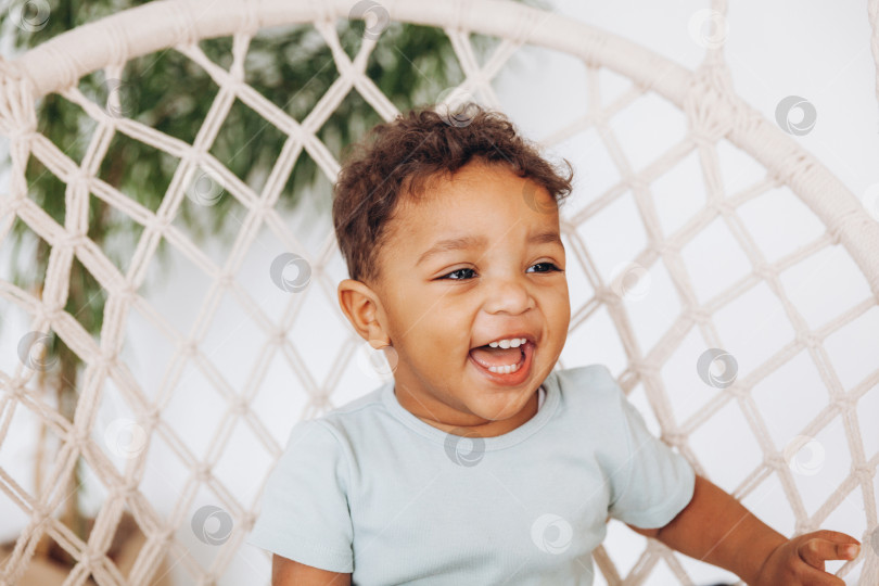 Скачать афроамериканский темнокожий ребенок сидит дома в подвесном кресле, счастливое летнее время. фотосток Ozero