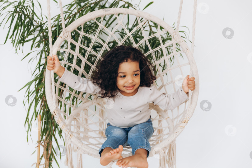 Скачать маленькая афроамериканская девочка в плетеном кресле, висящем в гостиной. фотосток Ozero
