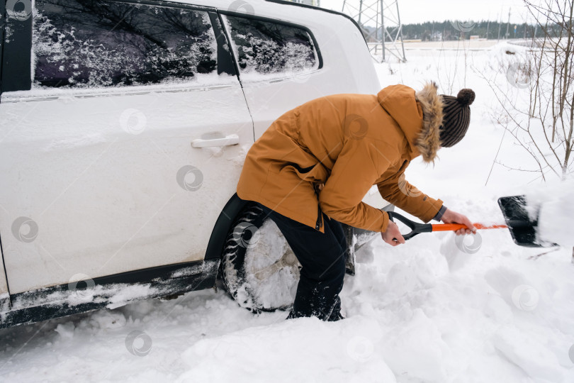Скачать Мужчина выкапывает заглохшую машину из снега автомобильной лопатой. Транспорт зимой застрял в сугробе после снегопада, сел на дно. Первая помощь, эвакуатор, шипы зимних шин и всесезонные фотосток Ozero