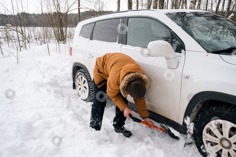 Скачать Мужчина выкапывает заглохшую машину из снега автомобильной лопатой. Транспорт зимой застрял в сугробе после снегопада, сел на дно. Первая помощь, эвакуатор, шипы зимних шин и всесезонные фотосток Ozero