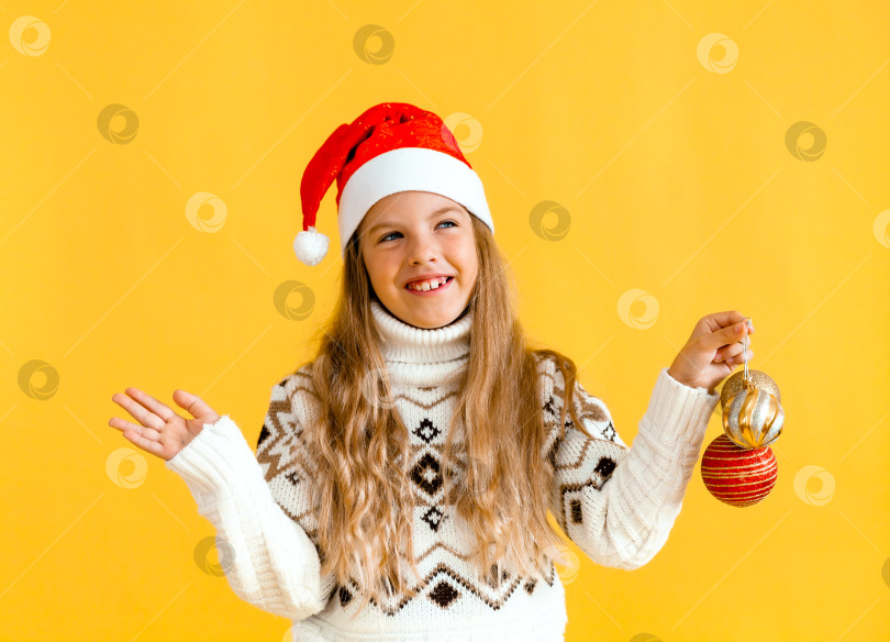 Скачать Украсьте рождественскую елку. маленькая белокурая девочка держит в руках рождественские шары. ребенок в новогодней шапочке держит в руках новогодние украшения. фотосток Ozero