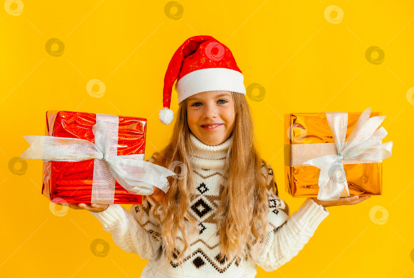 Скачать очаровательная маленькая девочка в вязаном свитере и шапочке Санты с подарком на желтом фоне. фотосток Ozero