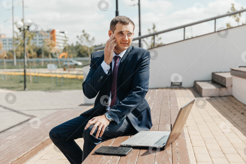 Скачать Мужчина в деловом костюме и с ноутбуком сидит на скамейке. бизнесмен с ноутбуком. фотосток Ozero