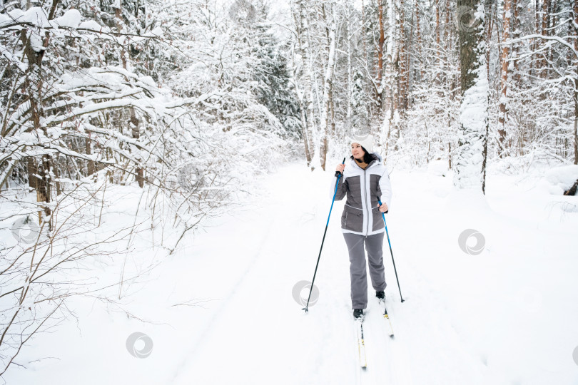Скачать Лыжница женщина в мембранной куртке с лыжными палками в руках спиной на фоне заснеженного леса. Катание на беговых лыжах в зимнем лесу, спорт на открытом воздухе, здоровый образ жизни. фотосток Ozero