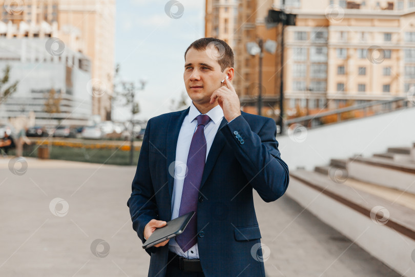 Скачать Молодой красивый бизнесмен в костюме разговаривает в наушниках. фотосток Ozero
