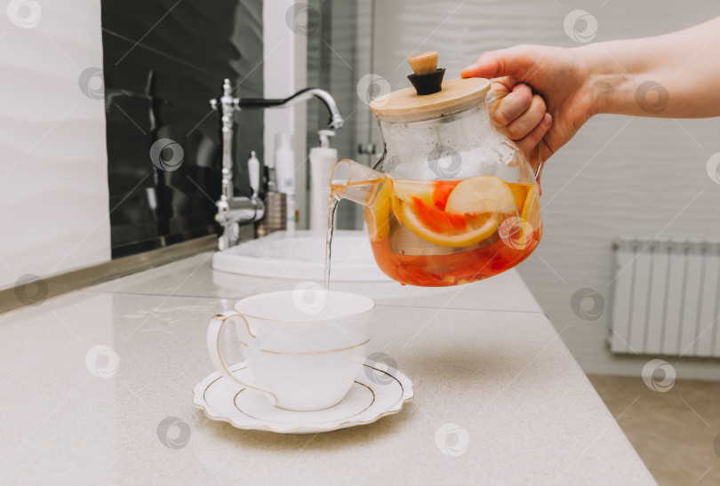 Скачать Процесс заваривания чая, чашка свежезаваренного фруктового и травяного чая, горячая вода наливается из чайника в чашку с заваркой. фотосток Ozero