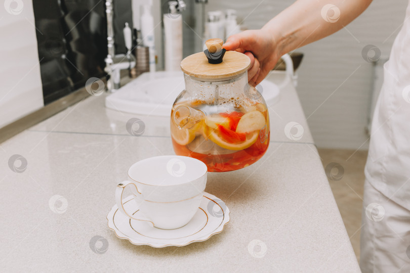 Скачать Процесс заваривания чая, чашка свежезаваренного фруктового и травяного чая, горячая вода наливается из чайника в чашку с заваркой. фотосток Ozero