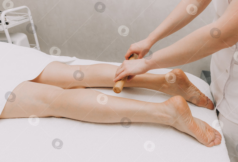 Скачать Женщина-массажист делает массаж ног и бедер бамбуковыми палочками. фотосток Ozero