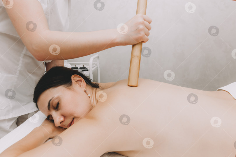 Скачать женщина делает массаж спины бамбуковой палочкой в оздоровительном спа-центре фотосток Ozero