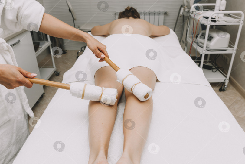 Скачать Женщина-массажист делает массаж ног и бедер бамбуковыми палочками. фотосток Ozero