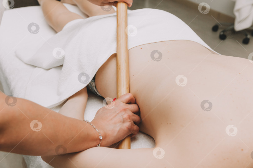 Скачать женщина делает массаж спины бамбуковой палочкой в оздоровительном спа-центре фотосток Ozero
