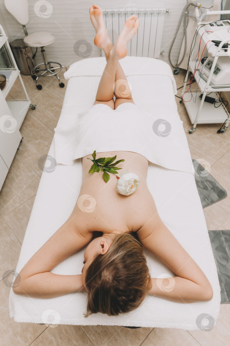 Скачать Молодая женщина наслаждается массажем в спа-салоне с белым цветком на спине. фотосток Ozero