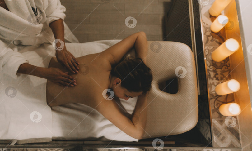 Скачать Уход за телом. Молодая девушка делает массаж, расслабляется в спа-салоне, вид сверху. фотосток Ozero