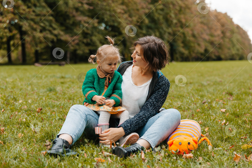 Скачать молодая женщина с ребенком на руках сидит на траве в парке. мама и дочь гуляют в парке. фотосток Ozero