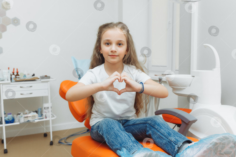 Скачать улыбающаяся маленькая девочка показывает сердечко руками в кресле стоматолога. фотосток Ozero