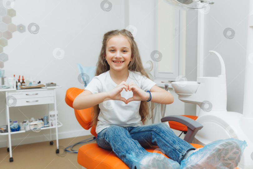 Скачать улыбающаяся маленькая девочка показывает сердечко руками в кресле стоматолога. фотосток Ozero