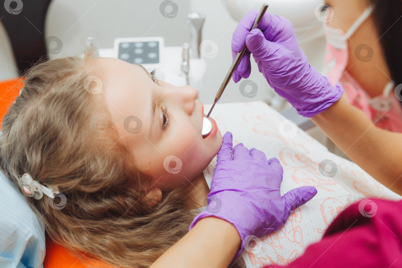 Скачать стоматолог проводит процедуру обследования милой маленькой девочки. Маленькая девочка сидит в кабинете дантиста фотосток Ozero
