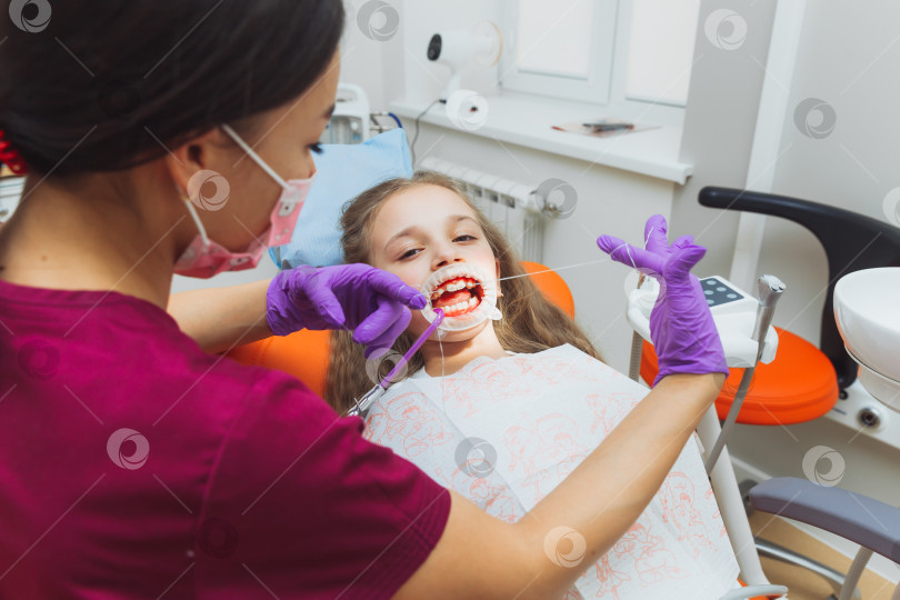 Скачать Стоматолог чистит зубы маленькой девочке зубной нитью. Фотография пациента с открытым ртом с резиновой прокладкой. фотосток Ozero