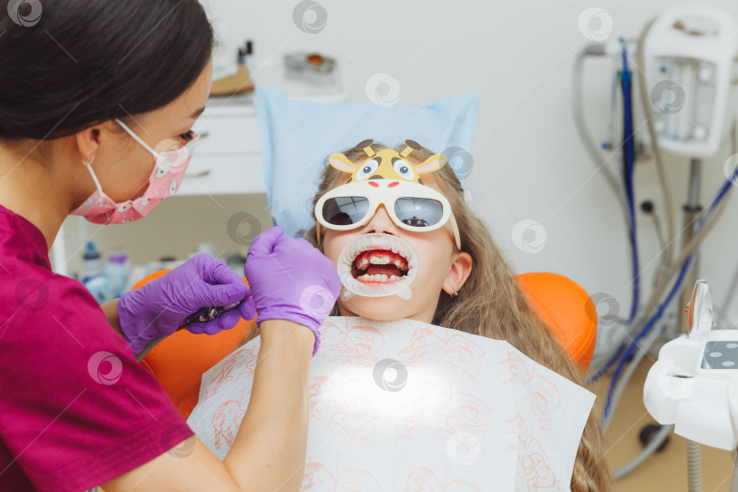 Скачать стоматолог использует резиновую прокладку во время осмотра пациента. маленькая девочка с втягивающим устройством для щеки во рту фотосток Ozero