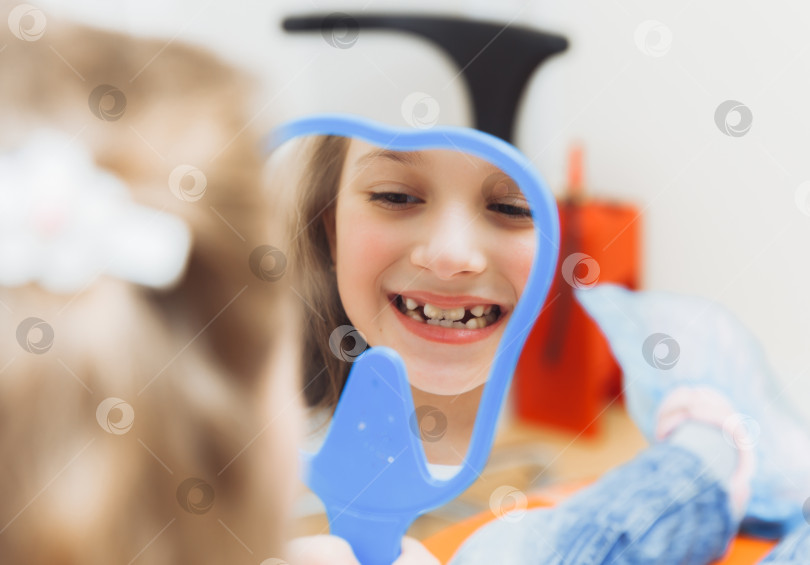Скачать Маленькая девочка сидит в стоматологическом кресле и рассматривает свои вылеченные зубы, глядя в зеркало фотосток Ozero