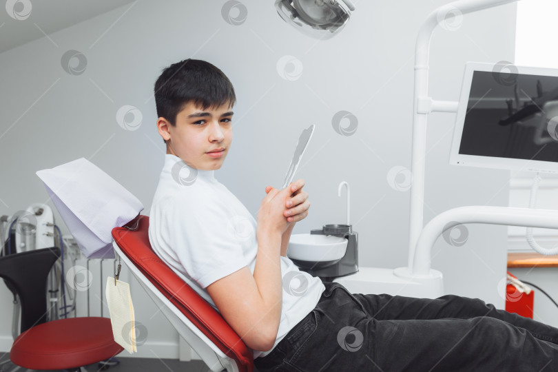 Скачать мальчик смотрится в зеркало с зубастой улыбкой, сидя на стуле рядом со стоматологом в стоматологическом кабинете. фотосток Ozero