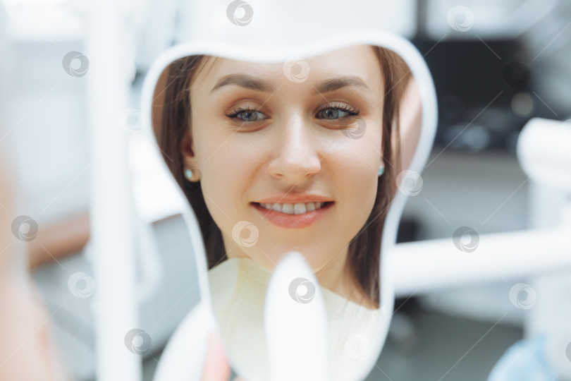 Скачать Молодая пациентка смотрит на свои зубы в зеркало. Современная стоматологическая клиника. отбеливание зубов фотосток Ozero