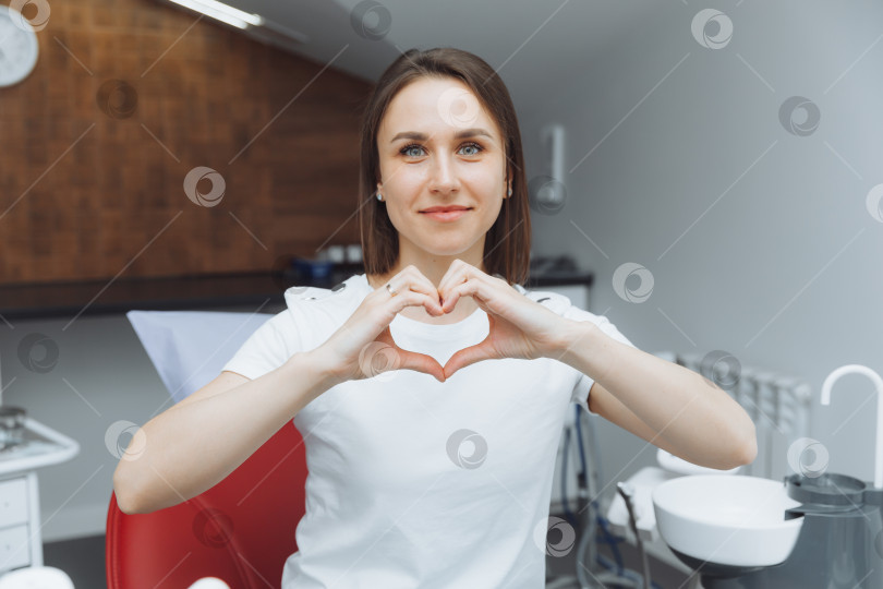 Скачать улыбающаяся молодая женщина, показывающая сердце руками в кресле стоматолога. фотосток Ozero