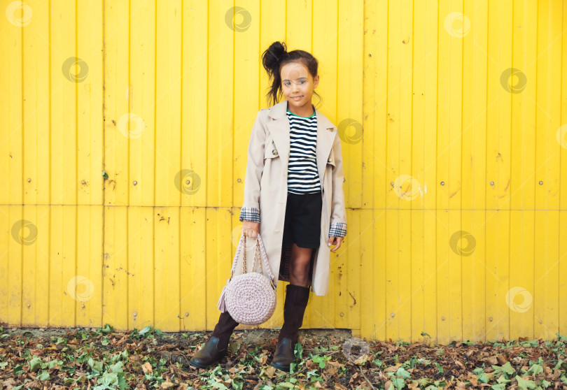 Скачать маленькая девочка в полосатой толстовке с капюшоном позирует на ярко-желтом заборе на улице. детская осенняя мода. поколение z.осень фотосток Ozero