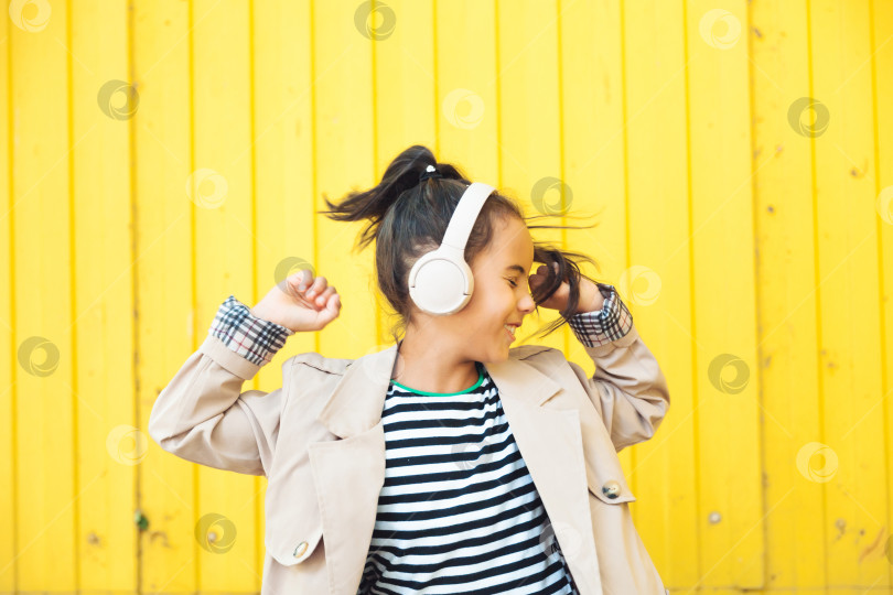 Скачать Желаю приятно провести время. Ребенок в наушниках слушает музыку. Концепция аудиокниги. Изучение аудио-уроков. маленькая девочка в наушниках слушает музыку. ребенок танцует на фоне желтого забора фотосток Ozero