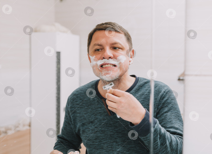 Скачать мужчина бреет бороду перед зеркалом в своей ванной комнате. фотосток Ozero