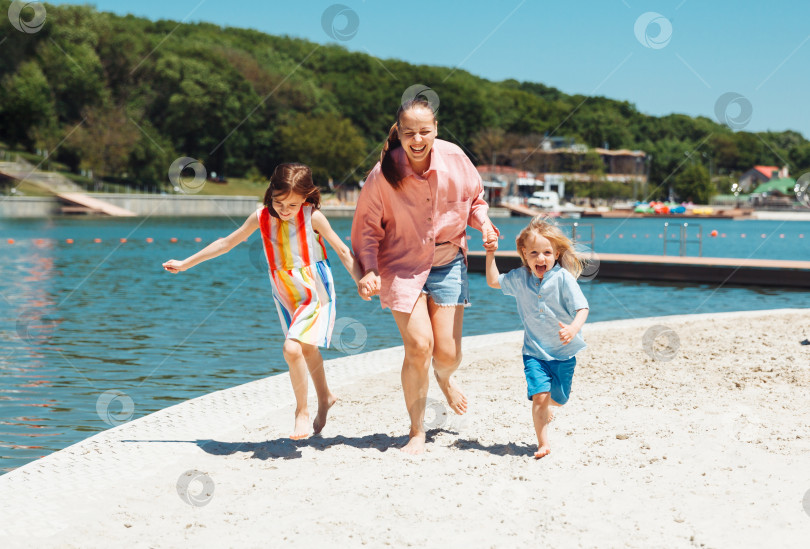 Скачать Мать и дети бегают и веселятся на пляже в дневное время. Концепция дружной семьи. фотосток Ozero