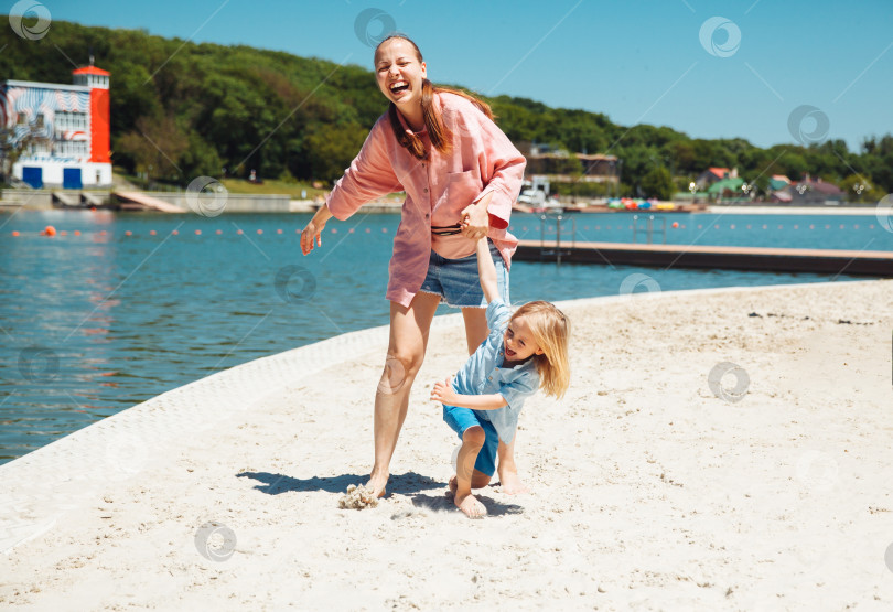 Скачать Портрет улыбающейся молодой матери с маленьким ребенком, бегущей по пляжу. летние каникулы.городской пляж фотосток Ozero