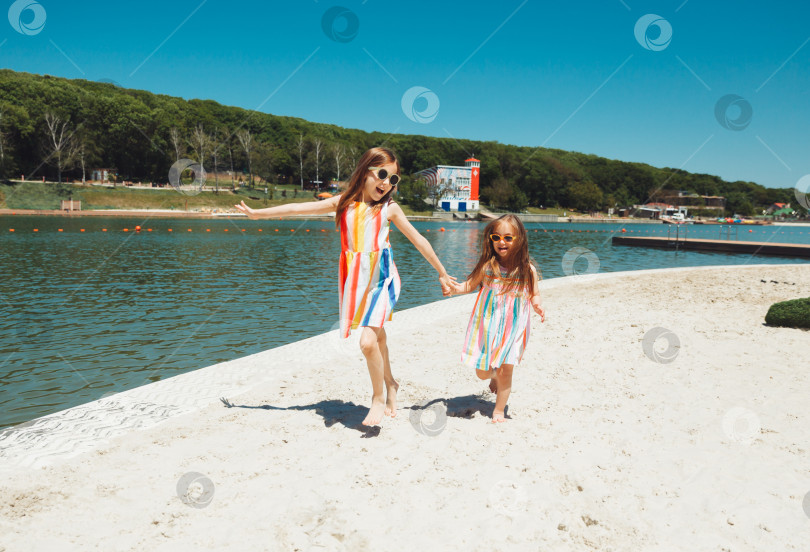 Скачать две счастливые маленькие девочки веселятся и радостно бегают по пляжу, прыгают по песку фотосток Ozero