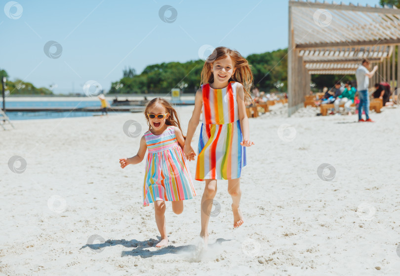 Скачать две счастливые маленькие девочки веселятся и радостно бегают по пляжу, прыгают по песку фотосток Ozero