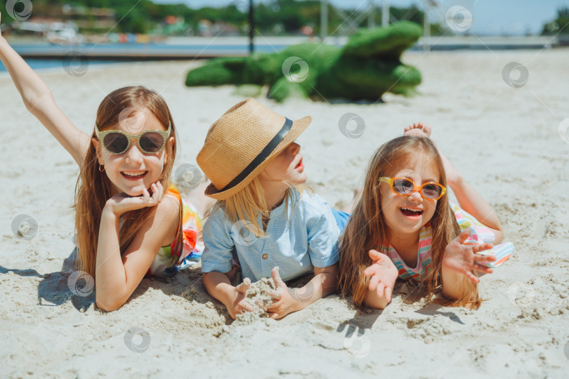 Скачать трое счастливых детей лежат на песке на пляже. ребенок с синдромом Дауна с друзьями веселится на пляже. фотосток Ozero