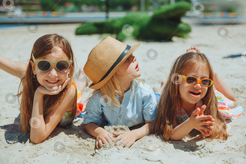 Скачать трое счастливых детей лежат на песке на пляже. ребенок с синдромом Дауна с друзьями веселится на пляже. фотосток Ozero