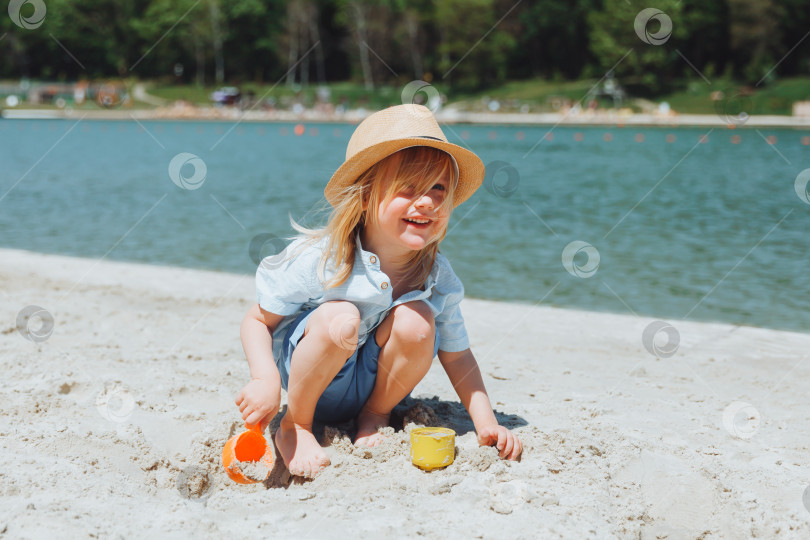 Скачать Милый счастливый светловолосый мальчик играет с пляжными игрушками на песчаном городском пляже. фотосток Ozero