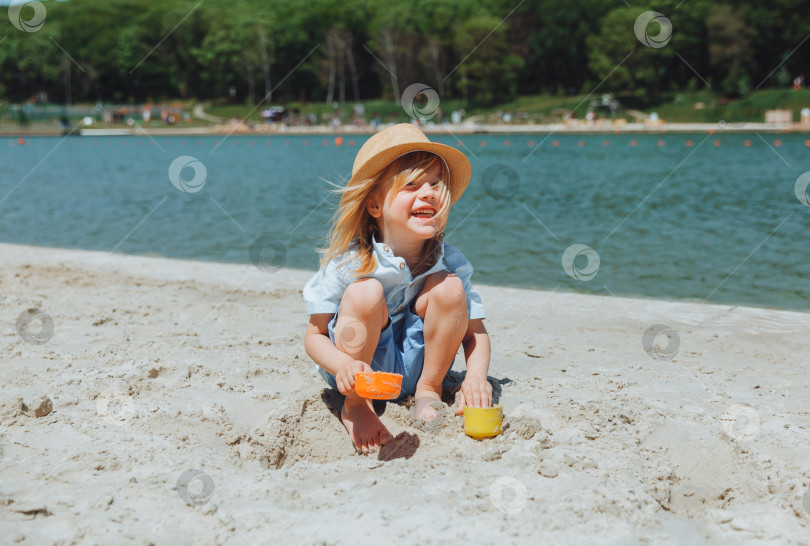 Скачать Милый счастливый светловолосый мальчик играет с пляжными игрушками на песчаном городском пляже. фотосток Ozero