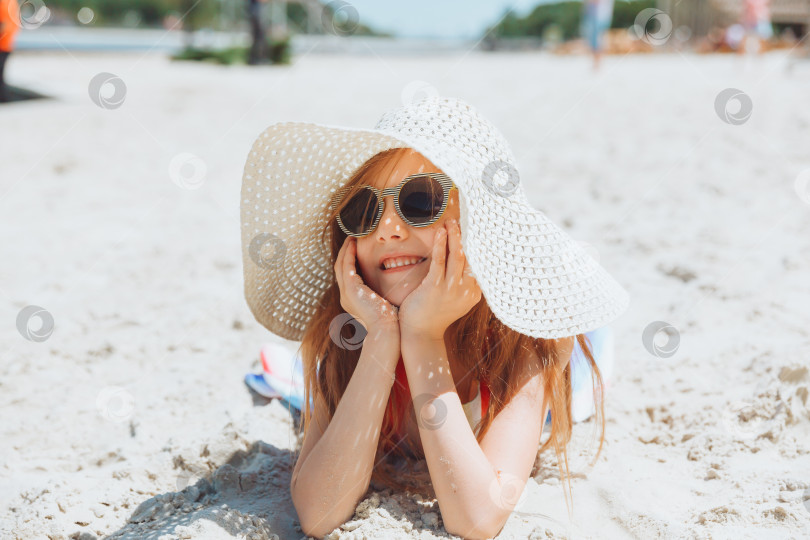 Скачать маленькая светловолосая девочка в соломенной шляпке лежит на песчаном пляже. девушка загорает на песке фотосток Ozero