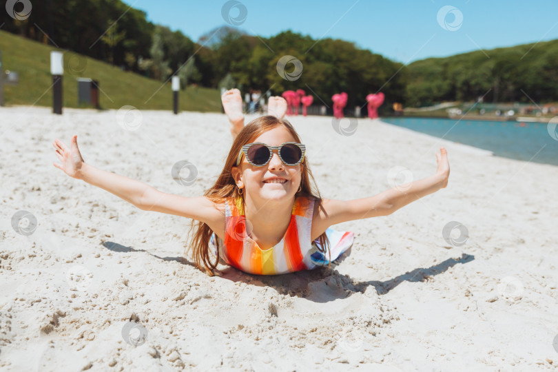 Скачать маленькая белокурая девочка в соломенной шляпке лежит на песчаном пляже. девушка загорает на песке фотосток Ozero