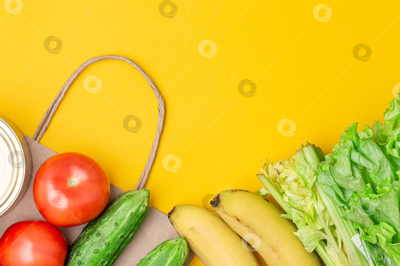 Скачать Бумажный пакет с продуктами, консервами, помидорами, огурцами, бананами, листьями салата на желтом фоне. фотосток Ozero