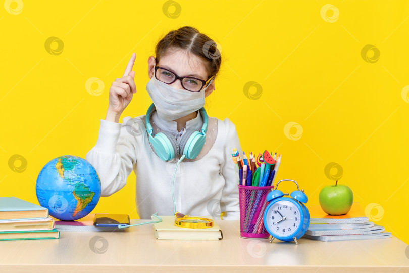 Скачать Школьница за своей партой в медицинской маске на желтом фоне фотосток Ozero