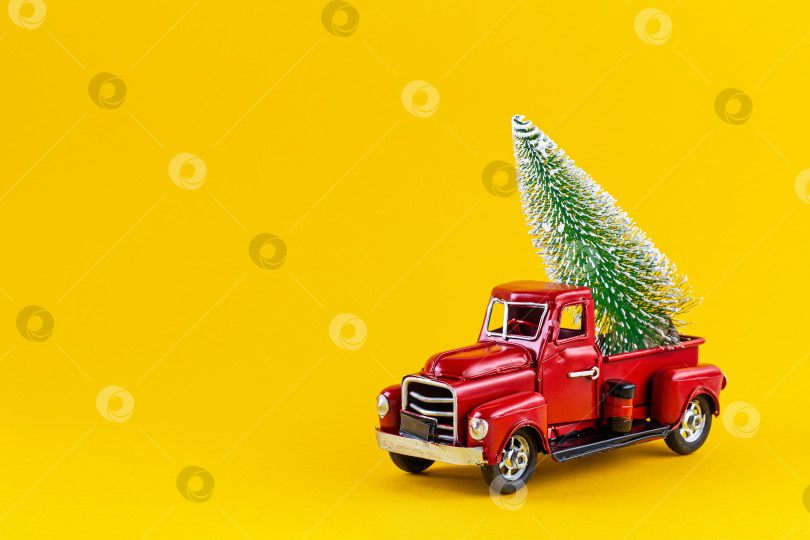 Скачать Красный ретро игрушечный грузовик с рождественской елкой на кузове грузовика на желтом фоне. фотосток Ozero