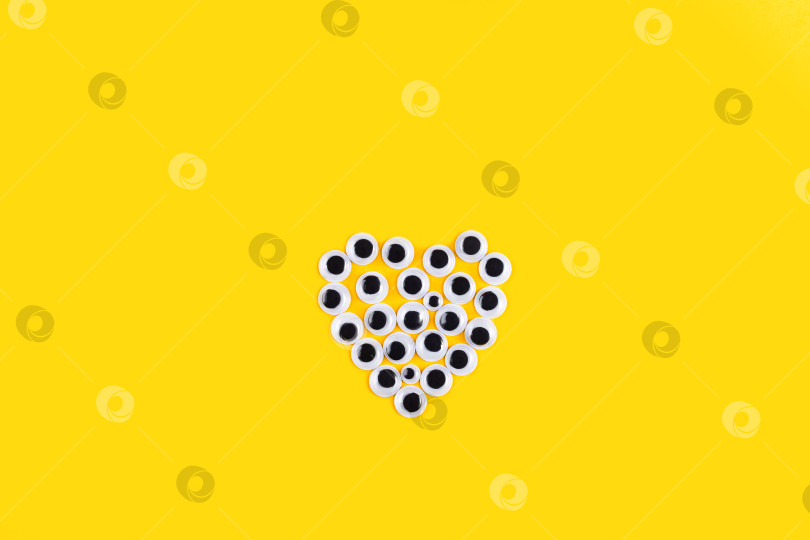 Скачать Форма сердца, выполненная из пластиковых глазок Googly на желтом фоне. фотосток Ozero
