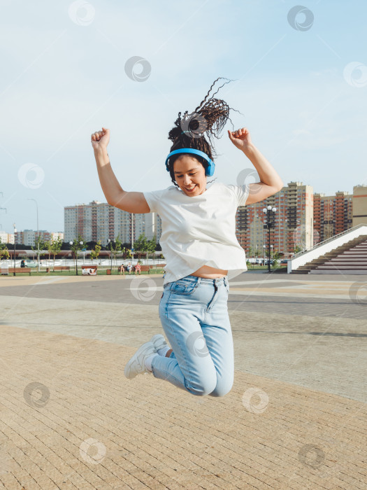 Скачать Жизнерадостная женщина слушает музыку через наушники на улице в солнечный день. девушка в наушниках прыгает по улице. поколение z фотосток Ozero